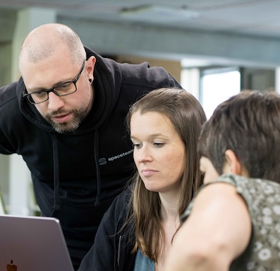 Three people looking at a notebook screen.